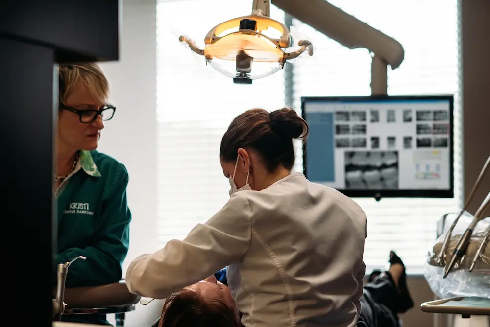 Dental assistant and patient during examination at Eugene dental practice with overhead surgical light.